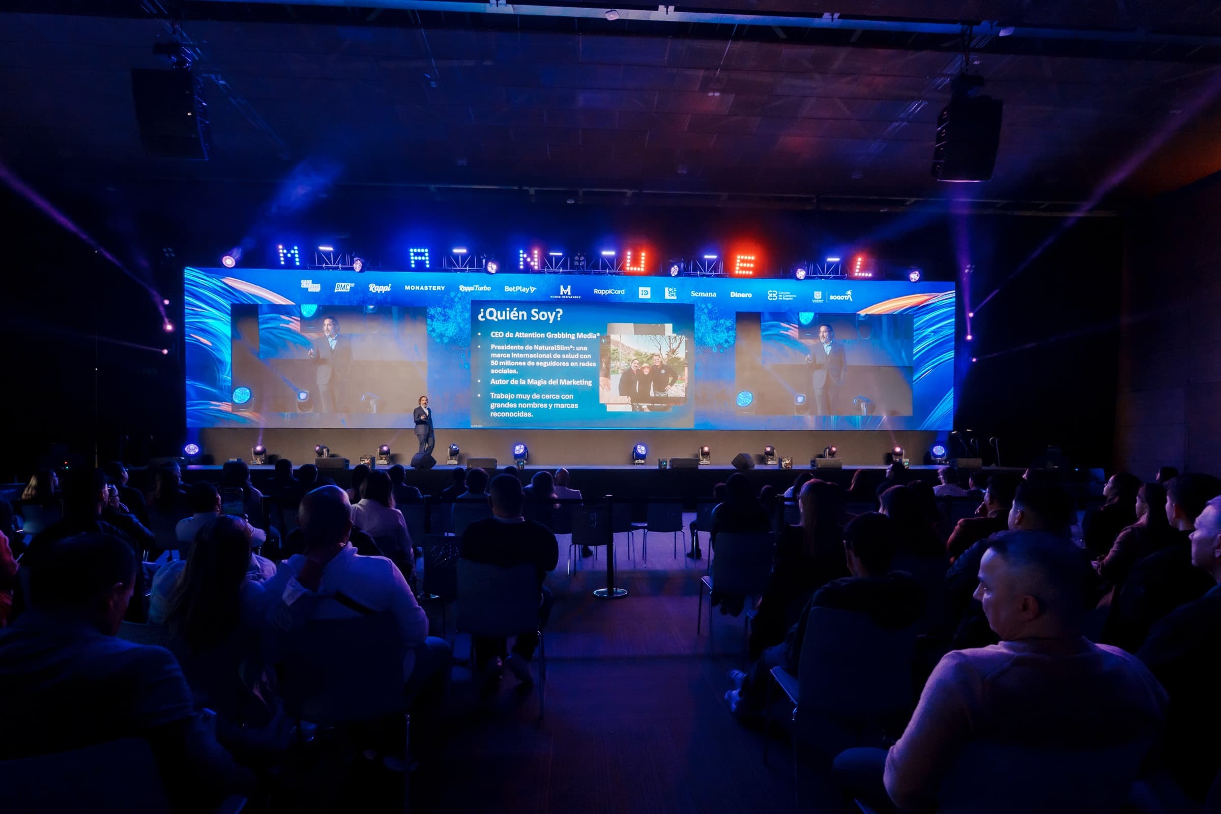 Wide view of a keynote arena at Game Changers Fest — Manuel Suarez on stage, his name spelled across the venue screen above a Spanish-language slide