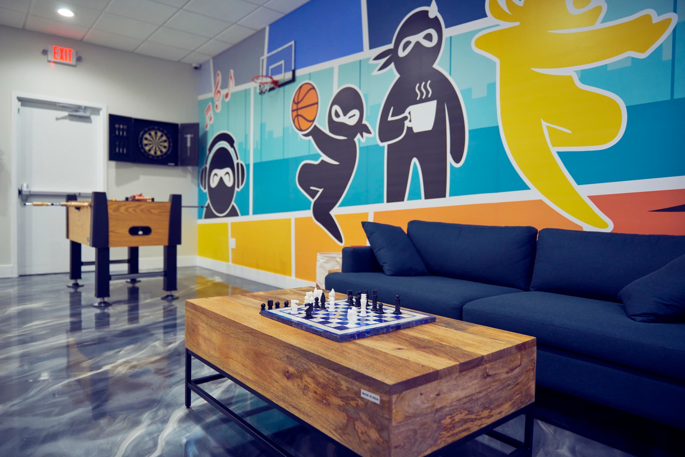 Game lounge with a comic-style ninja mural, foosball table, dartboard, and a chessboard on the coffee table