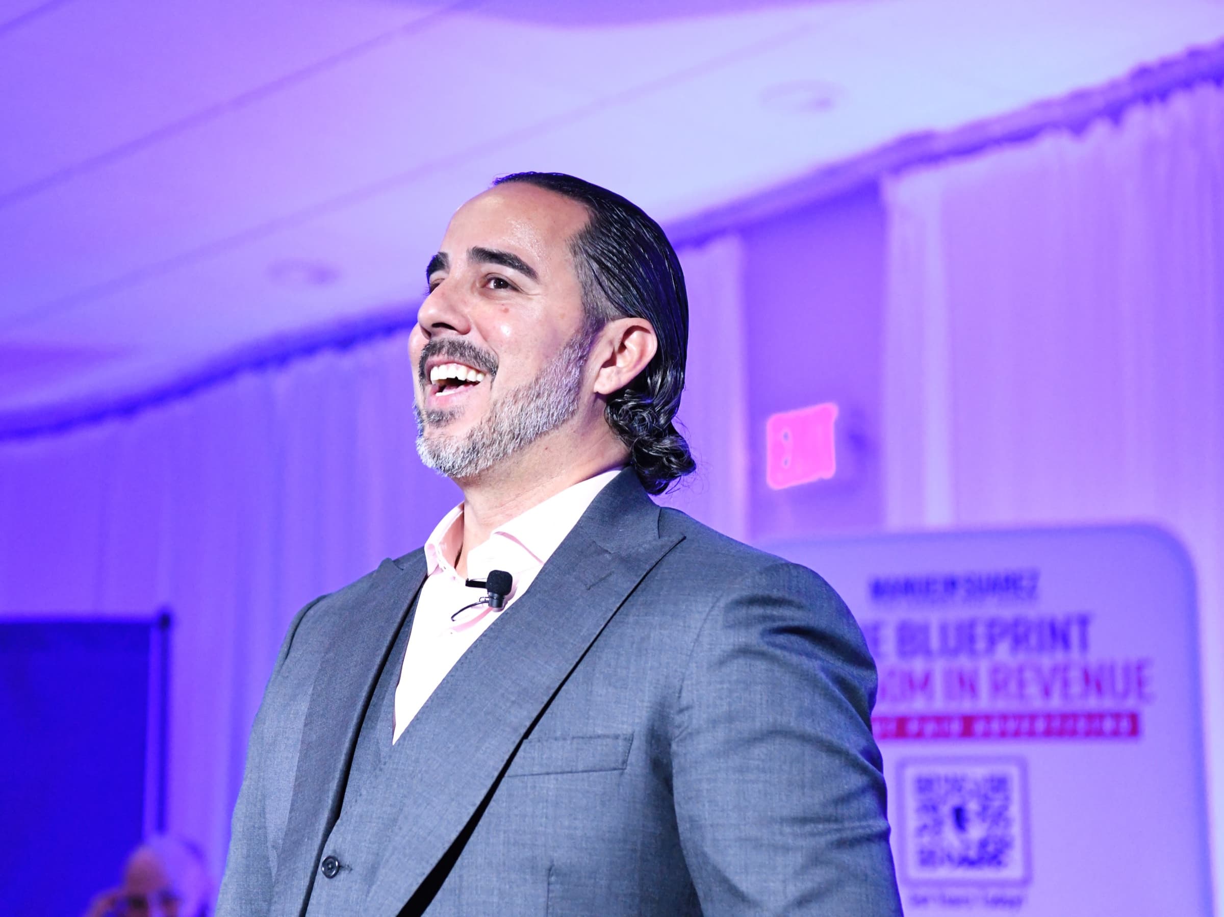 Manuel Suarez laughing on a purple-lit stage at the Marketing Magic launch event