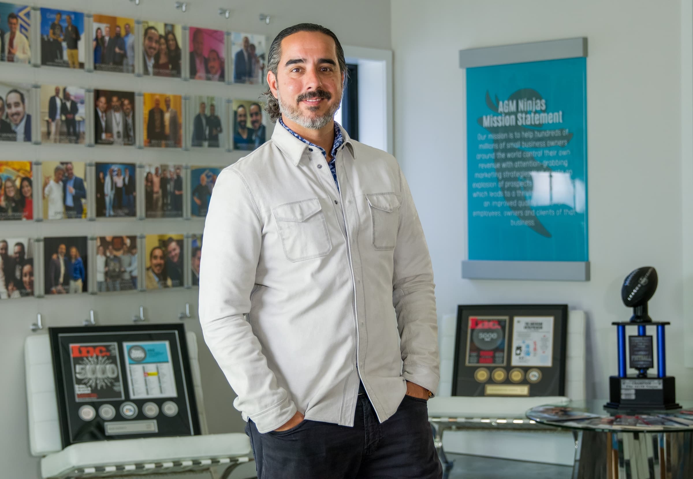 Manuel Suarez beside the AGM mission-statement wall with framed awards