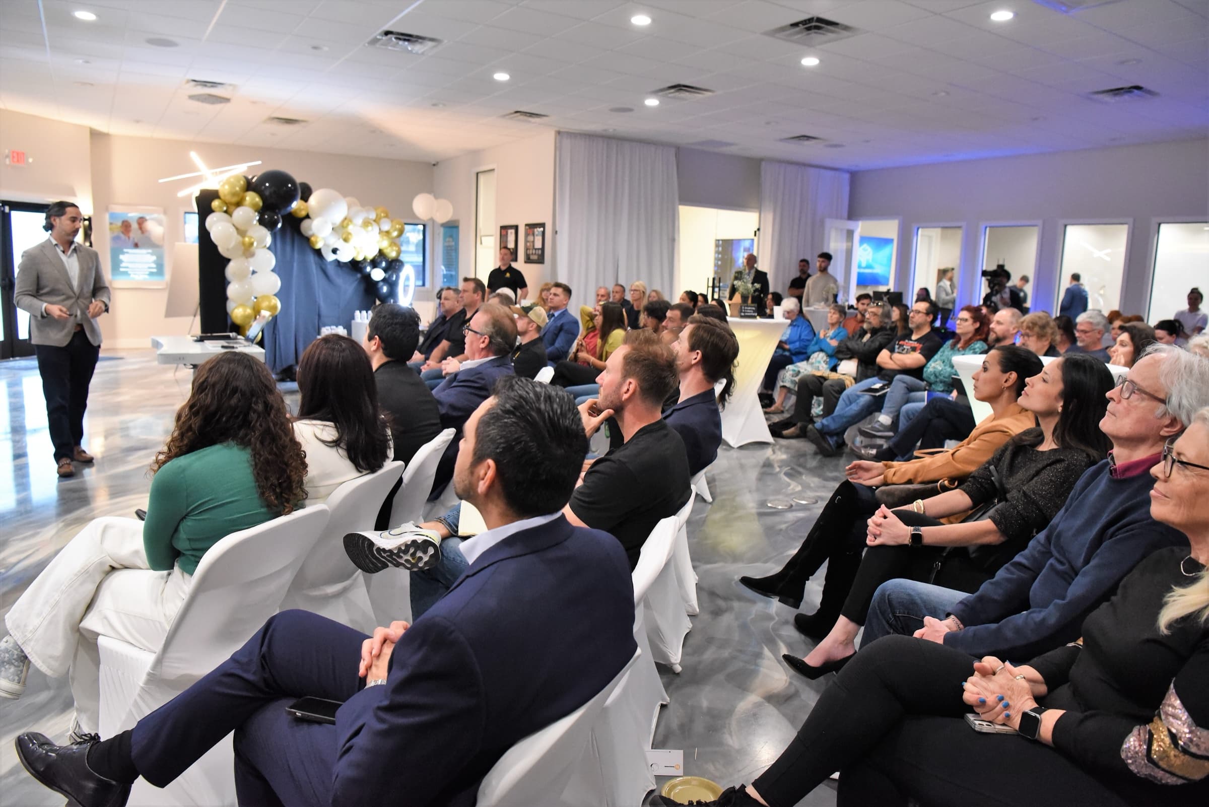Side view of a packed audience with the speaker at the front of the room