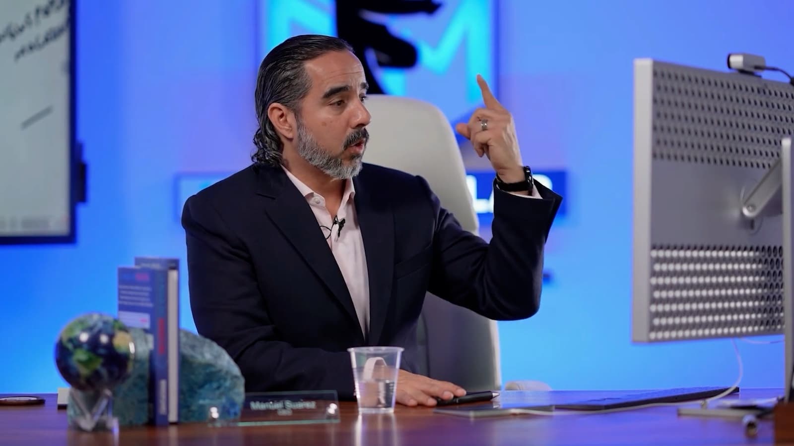 Manuel recording his desk show, lav mic on, monitor at hand, branded backdrop